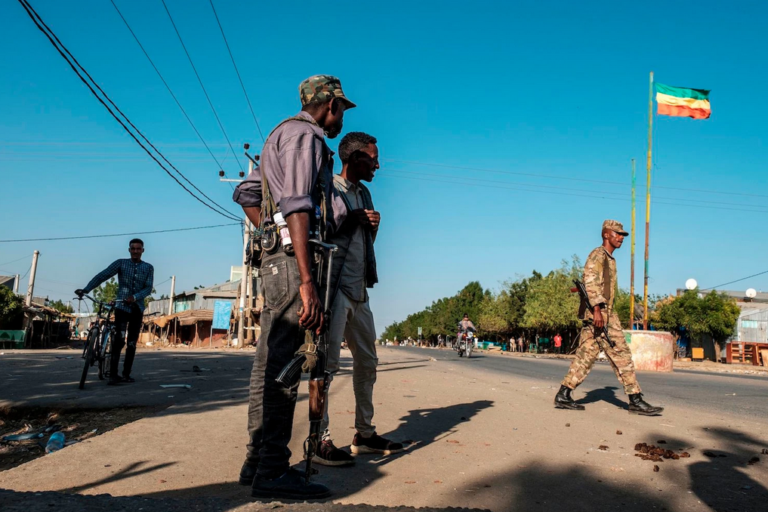 I membri della milizia Amhara si trovano in una strada mentre un soldato cammina davanti a una bandiera imperiale etiope, a Mai Kadra, in Etiopia, il 21 novembre 2020